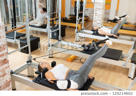 Girl performing legs exercise using straps on Pilates reformer 120214602