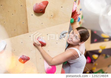 Sporty woman exercising on wall in climbing gym during bouldering training 120214604