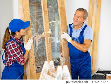 Woman and man repairers carrying new door in apartment Woman and man repairers carrying new door in apartment 120214636