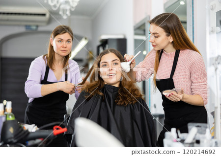 Make-up artist and a hairdresser serve a young female client 120214692