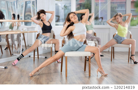 Group of women in high heels rehearsing dance while sitting on chair 120214819