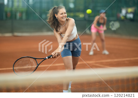 Girl swinging racket to hit ball during tennis doubles on outdoor court 120214821