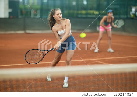 Two young women playing doubles tennis 120214824
