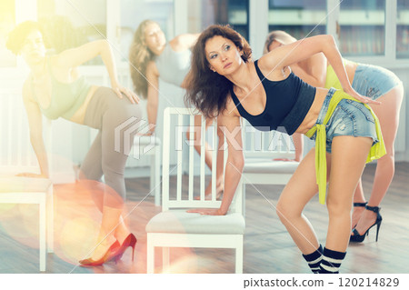 Positive beautiful flexible woman practicing emotive movements near chair, combined with grace of high heels during group dance class in sports studio Positive beautiful flexible woman practicing emotive movements near chair, combined with grace of high heels during group dance class in sports studio 120214829