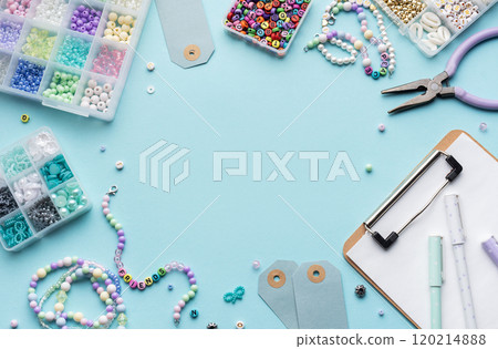 Colorful beads, pliers, clipboard and price tags arranged on blue surface for diy bracelet making 120214888