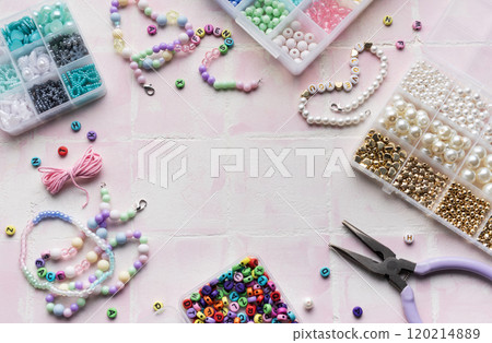 Colorful beads and jewelry making tools arranged on pink tile surface 120214889