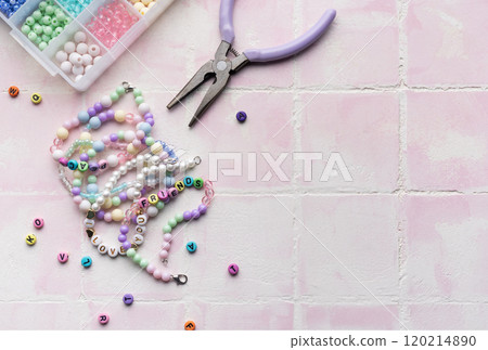Colorful beads and jewelry making tools arranged on pink tile surface Colorful beads and jewelry making tools arranged on pink tile surface 120214890