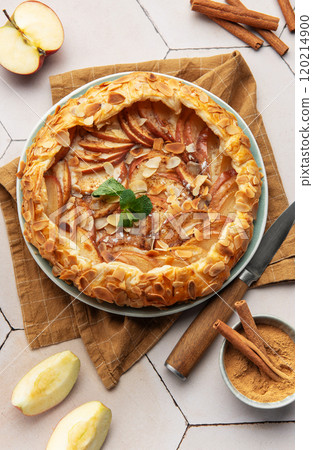 Delicious apple galette decorated with almond petals and cinnamon sticks on white table 120214900