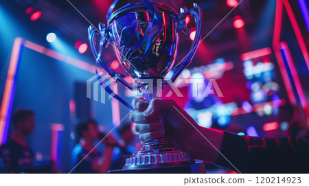 Silver trophy cup held up in vibrant esports arena lighting, symbol of victory and teamwork in gaming cyber sport competition 120214923