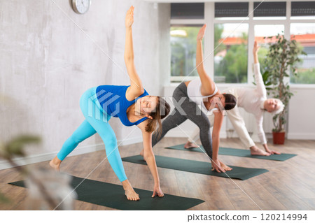 Sporty woman doing standing forward bend Uttanasana, effective yoga pose for back flexibility in group workout 120214994