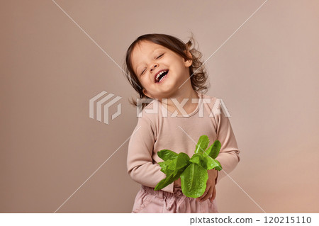 cute child girl holding fresh green salad on beige background. healthy baby food. cute child girl holding fresh green salad on beige background. healthy baby food. 120215110
