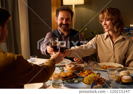Medium close up of happy friends sitting at festive table with treats, drinking red wine and enjoying company 120215247