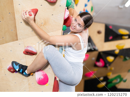 Young Europian woman climbs steep artificial wall in sports complex and trains endurance 120215270