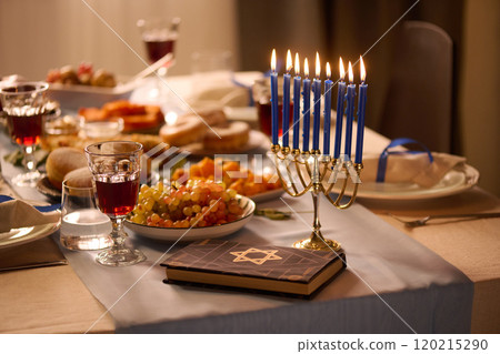 Medium close up of lit blue candles next to Torah on table with huge number of traditional treats and alcoholic beverages Medium close up of lit blue candles next to Torah on table with huge number of traditional treats and alcoholic beverages 120215290