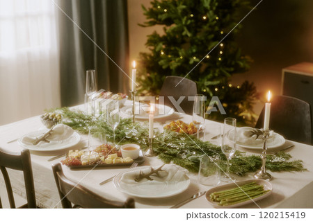 High angle shot of decorated table with appetizers, fur tree with golden lights in dining room 120215419