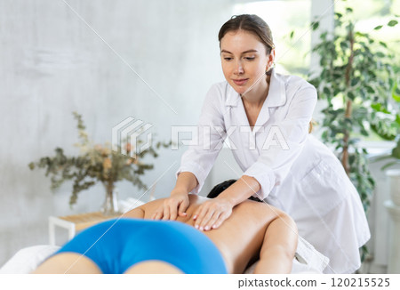 Professional young masseuse performing back massage for male patient Professional young masseuse performing back massage for male patient 120215525