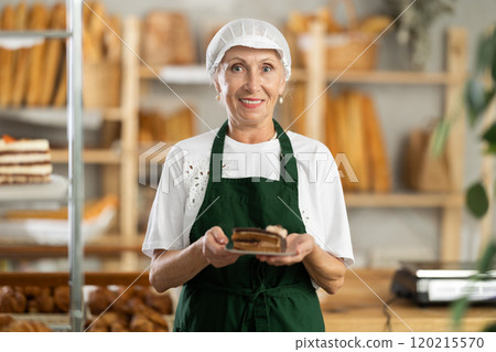 Mature saleswoman offering a piece of cake in plate in bakery Mature saleswoman offering a piece of cake in plate in bakery 120215570