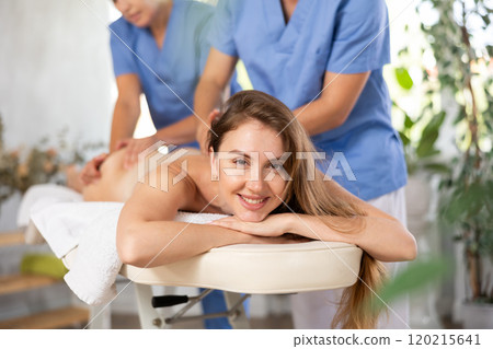 Two unrecognizable female and male masseuses perform stroking and rubbing of muscle of back to girl Two unrecognizable female and male masseuses perform stroking and rubbing of muscle of back to girl 120215641