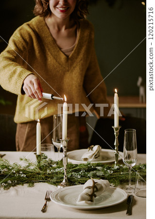 Vertical shot of unrecognizable beaming woman in yellow sweater lighting up candle in silver candlestick Vertical shot of unrecognizable beaming woman in yellow sweater lighting up candle in silver candlestick 120215716