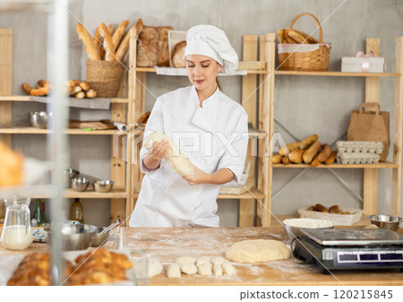 Process of making baguette, loaf or bread in bakery - female baker kneads and rolls dough to give shape of future bread 120215845
