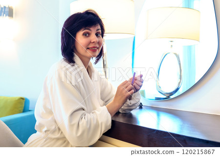 A pleasant morning at the hotel - a woman preens herself near the mirror 120215867