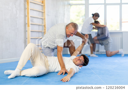 Two men at group judo lesson practicing techniques in sparring, in background men are practicing techniques too 120216004