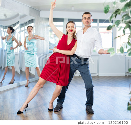 Woman in red dancing passionate bachata with man at dance class Woman in red dancing passionate bachata with man at dance class 120216100