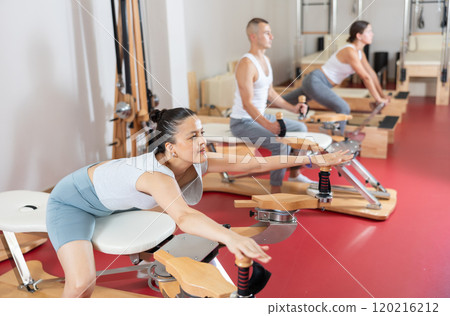 Young woman stretching her arms using pilates machine Young woman stretching her arms using pilates machine 120216212