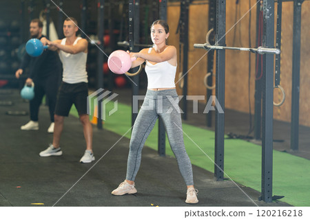 Sportive young woman lifting heavy kettlebell in sports hall 120216218