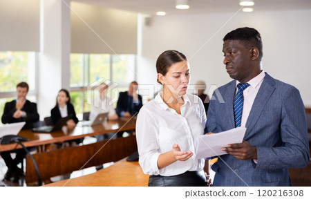 Middle aged african male manager discussing report with a young white dark-haired subordinate female worker 120216308