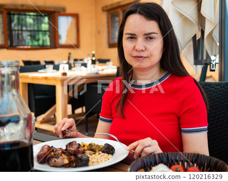 Portrait of woman spending time on open terrace of restaurant and eating traditional parillada de carne Portrait of woman spending time on open terrace of restaurant and eating traditional parillada de carne 120216329