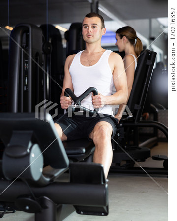Sportive young guy training his arms using cable exercise machine in gym Sportive young guy training his arms using cable exercise machine in gym 120216352
