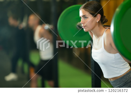 Fit girl doing exercises with barbell during group workout Fit girl doing exercises with barbell during group workout 120216372