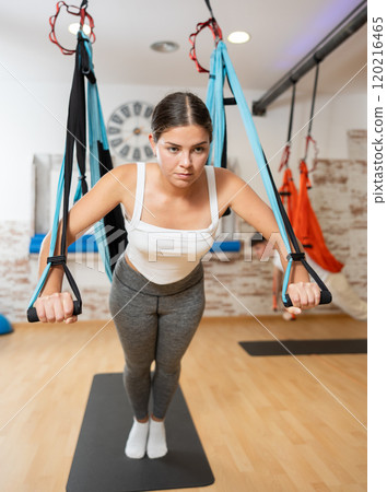 Girl visitor performs exercises in hanging position on Pilates slings hammock 120216465
