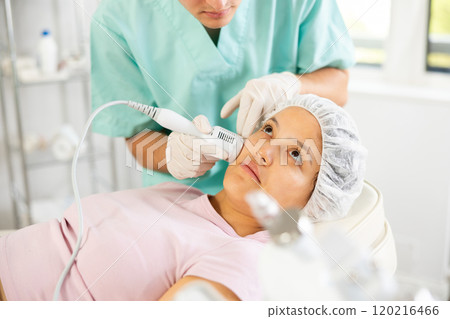 Young male cosmetologist doing whitening procedure to young woman 120216466