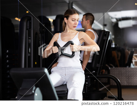 Sportive young girl training her arms using cable exercise machine in gym 120216478