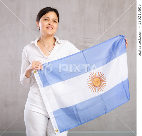 Middle-aged positive woman holds unfurled flag of Argentina in hands raised above head 120216609