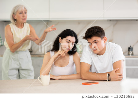 Mature mom make claims to young couple in home kitchen 120216682