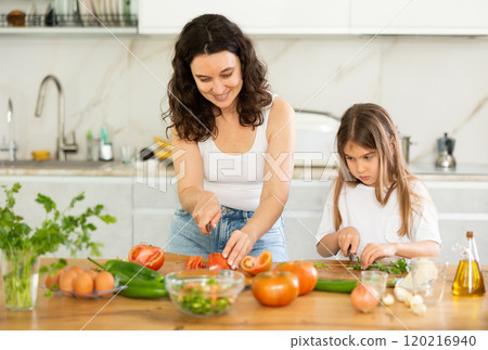 Mom and daughter dice up raw vegetables for salad on cutting boards. 120216940