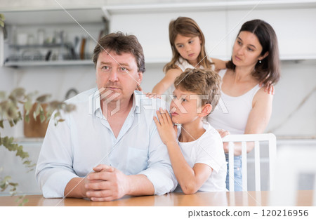 Frustrated man sits at kitchen table and tells wife and children about unforeseen difficulties 120216956