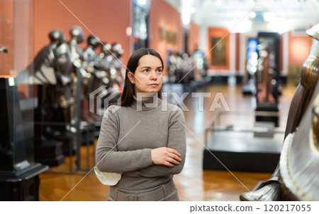 Interested female tourist visiting exhibition of medieval armor in museum Interested female tourist visiting exhibition of medieval armor in museum 120217055