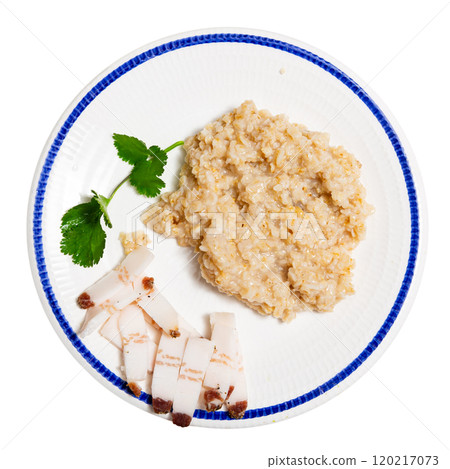 There is portion of boiled oatmeal porridge with pieces of salted bacon on plate. There is portion of boiled oatmeal porridge with pieces of salted bacon on plate. 120217073