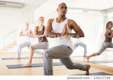 Hispanic man practicing Parvritta Parsvakonasana during group yoga training Hispanic man practicing Parvritta Parsvakonasana during group yoga training 120217190