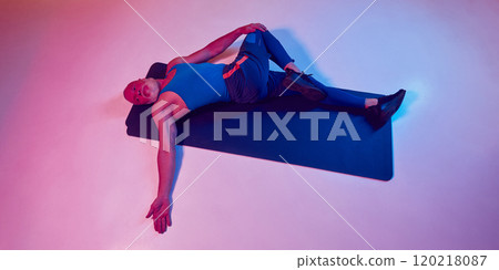 Top view image of elderly athletic man in sportswear, lying on fitness mat and stretching body against gradient pink background in neon light 120218087