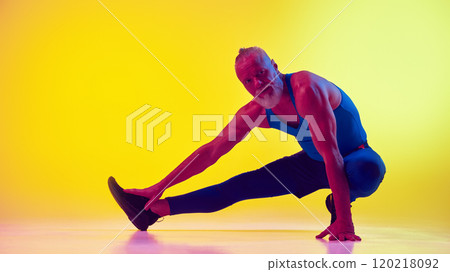 Elderly man with muscular strong body, in sportswear training, doing stretching exercises against gradient yellow background in neon light Elderly man with muscular strong body, in sportswear training, doing stretching exercises against gradient yellow background in neon light 120218092