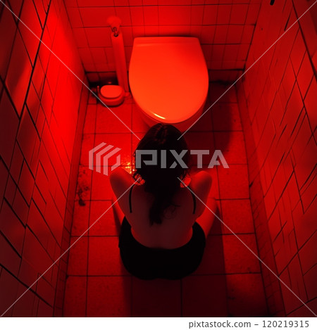 Woman sitting on floor in red lit bathroom feeling despair 120219315