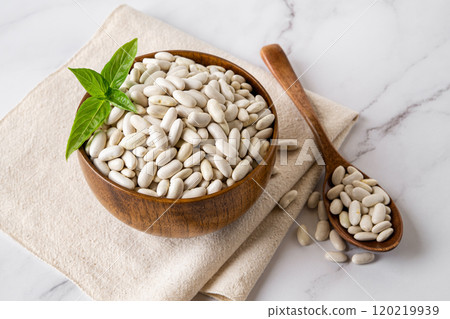 White beans in a wooden bowl and spoon over marble surface.  White beans in a wooden bowl and spoon over marble surface.  120219939