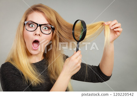 Woman holding magnifying glass looking at hair 120220542