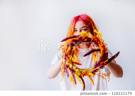 Portrait of young Caucasian woman with playful expression, vibrant red and orange hair holding colorful autumn wreath against white background. Creativity and joy, autumn leaves, artistic vibe. Portrait of young Caucasian woman with playful expression, vibrant red and orange hair holding colorful autumn wreath against white background. Creativity and joy, autumn leaves, artistic vibe. 120222179