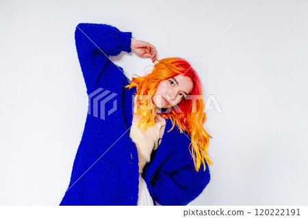 Young woman with vibrant orange hair wearing blue sweater, leaning against white wall. Thoughtful expression, life's meaning, depression. Self-discovery, feelings of vulnerability and contemplation. Young woman with vibrant orange hair wearing blue sweater, leaning against white wall. Thoughtful expression, life's meaning, depression. Self-discovery, feelings of vulnerability and contemplation. 120222191